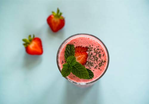 A strawberry smoothie glass with two halves of a strawberry on a table.