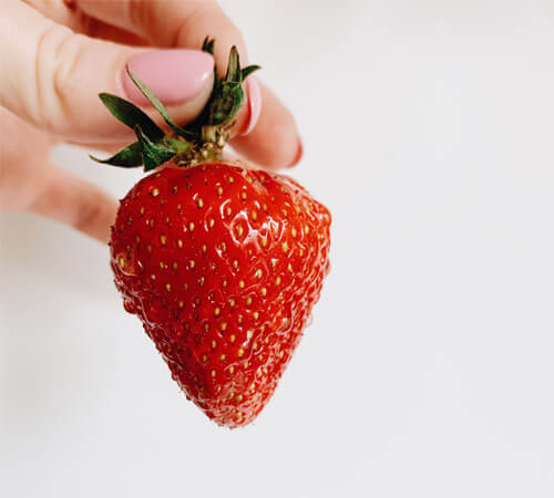 Hand holding a strawberry by the stem in front of a white background.